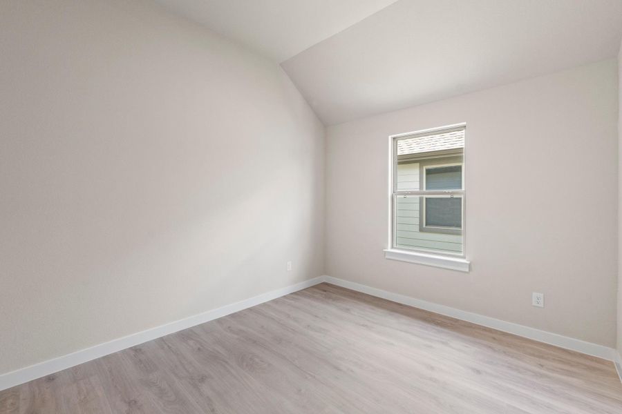 A well-lit bedroom features durable laminate flooring and a peaked ceiling.