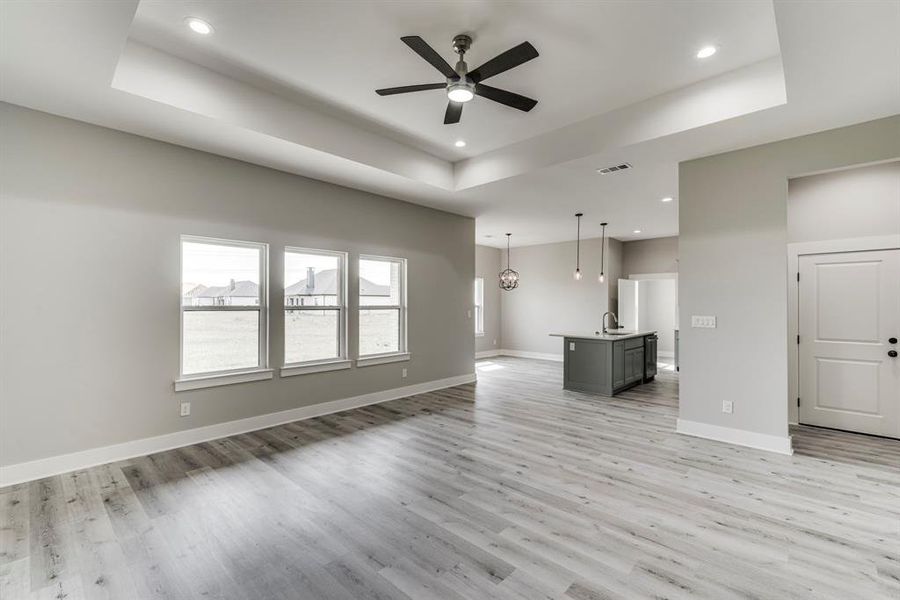 Unfurnished living room with light hardwood / wood-style floors, ceiling fan, and a raised ceiling