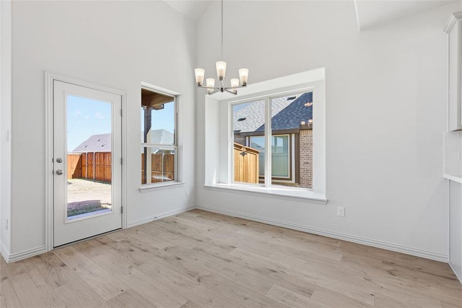 Spacious room featuring vaulted ceilings, light wood-finish flooring, and crisp white walls