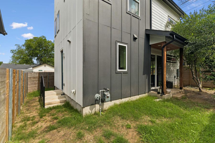 Exterior featuring vertical panel siding in a two-tone gray and white finish, a covered patio with wood support beams, and a wood privacy fence