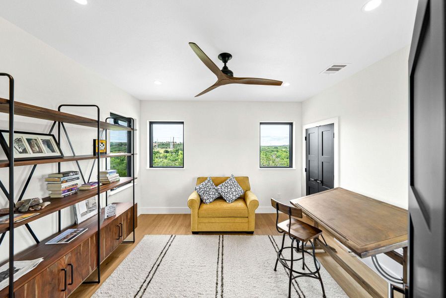 Rich hardwood flooring and minimalist black-framed windows frame views of the surrounding green hillsides.
