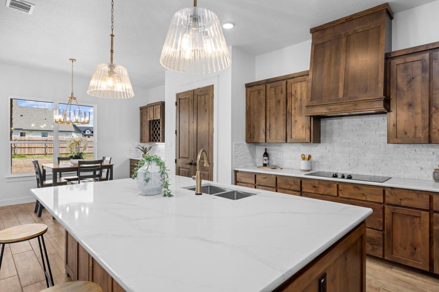Kitchen featuring a center island with sink, light stone counters, wood finish floors, a breakfast bar, and backsplash