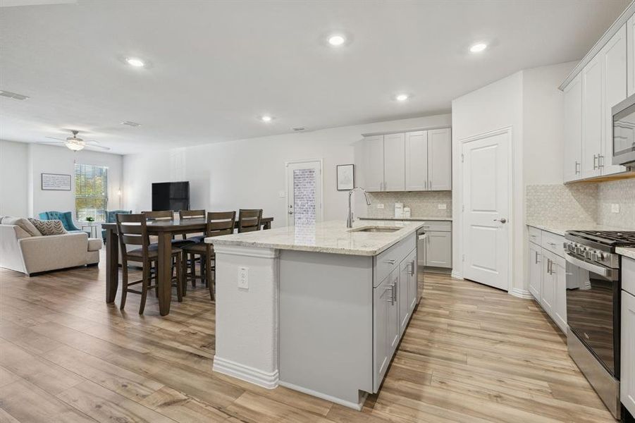 Kitchen featuring open floor plan, light stone countertops, appliances with stainless steel finishes, an island with sink, and light wood-style floors