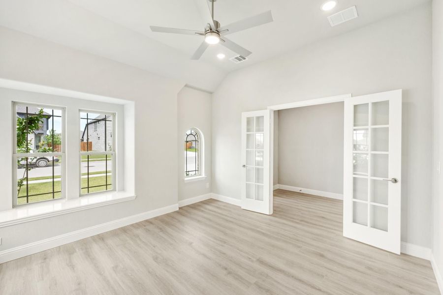 Empty room with vaulted ceiling, ceiling fan, light wood floors, and white French doors Empty room with vaulted ceiling, ceiling fan, light wood floors, and white French doors