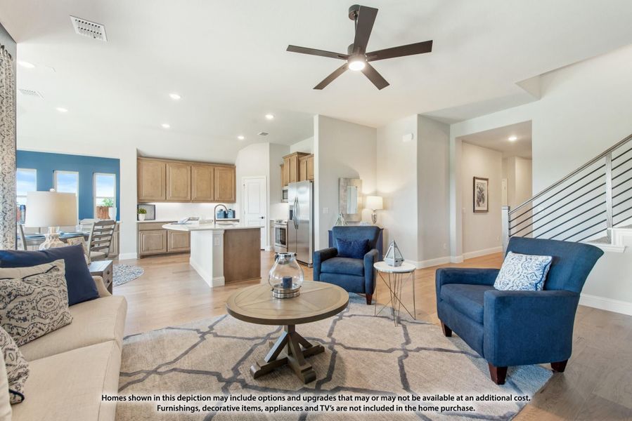 Open-concept living room with ceiling fan flowing into kitchen with island and stainless appliances, hardwood floors throughout Open-concept living room with ceiling fan flowing into kitchen with island and stainless appliances, hardwood floors throughout
