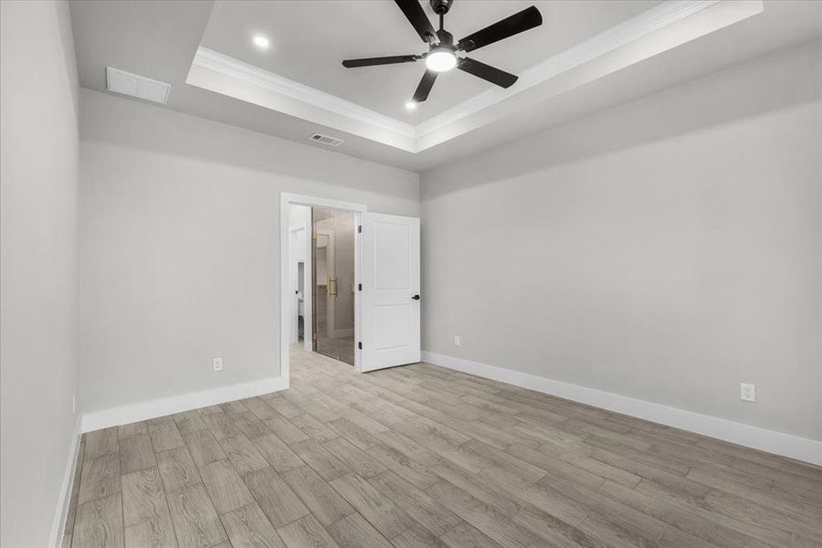 Empty room with crown molding, a raised ceiling, visible vents, wood finished floors, and baseboards