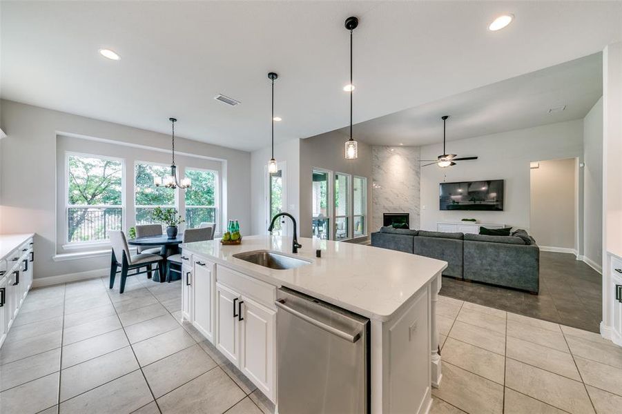 Kitchen featuring stainless steel dishwasher, hanging light fixtures, sink, white cabinets, and a kitchen island with sink