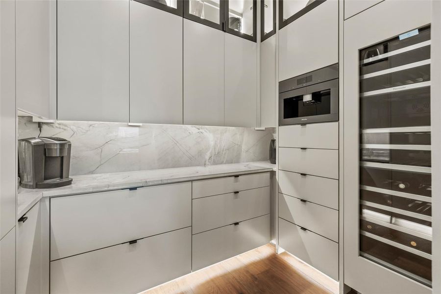 Integrated kitchen featuring light gray cabinetry, an undermount built-in coffee maker, and a full-height wine refrigerator