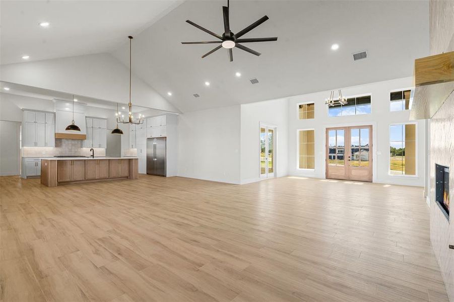 Unfurnished living room with a chandelier, high vaulted ceiling, light wood-style floors, a fireplace, and a ceiling fan Unfurnished living room with a chandelier, high vaulted ceiling, light wood-style floors, a fireplace, and a ceiling fan