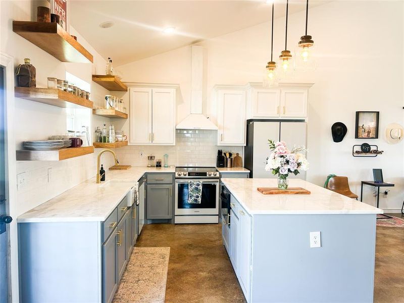 Kitchen with concrete flooring, decorative backsplash, appliances with stainless steel finishes, light stone countertops, and a kitchen island Kitchen with concrete flooring, decorative backsplash, appliances with stainless steel finishes, light stone countertops, and a kitchen island