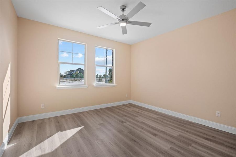 Room featuring two windows, neutral wall color, contemporary ceiling fan with integrated lighting, wood-finish flooring, and white baseboards Room featuring two windows, neutral wall color, contemporary ceiling fan with integrated lighting, wood-finish flooring, and white baseboards