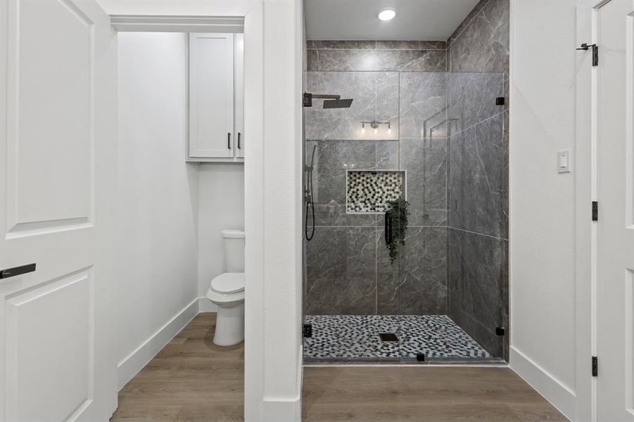 Full bath with baseboards, wood finished floors, toilet, and a stall shower