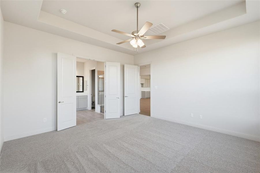 Unfurnished bedroom featuring a raised ceiling, light colored carpet, ceiling fan, and connected bathroom Unfurnished bedroom featuring a raised ceiling, light colored carpet, ceiling fan, and connected bathroom