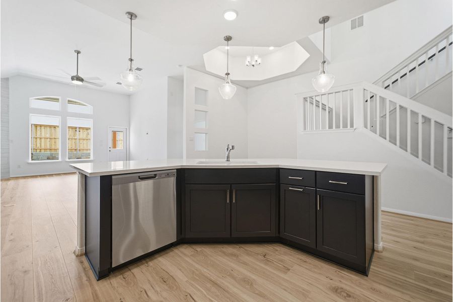 Kitchen with an island with sink, stainless steel dishwasher, light wood-style floors, and pendant lighting