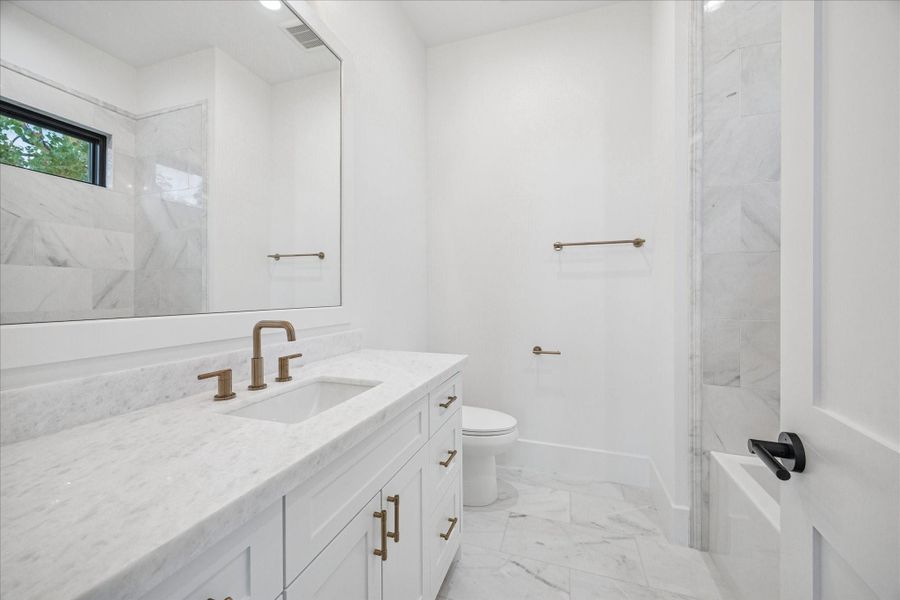 Marble tile climbs the wall while a wide window provides natural light and privacy. Brass fixtures warm the clean palette. Marble tile climbs the wall while a wide window provides natural light and privacy. Brass fixtures warm the clean palette.