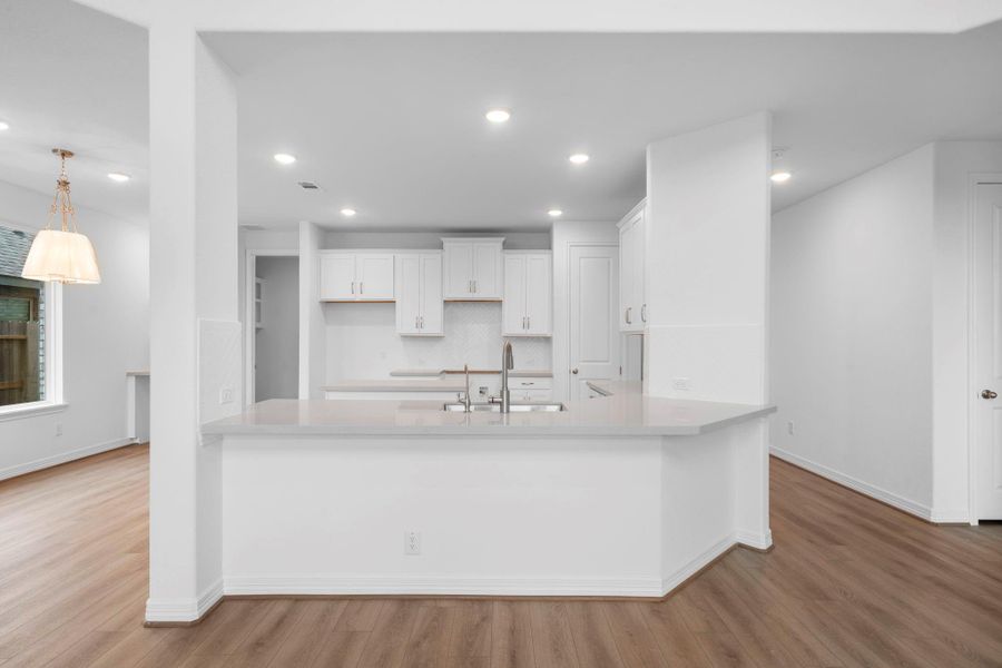 This light and bright kitchen features a large quartz island, white cabinets, a large sink overlooking your family room, recessed lighting, and beautiful backsplash.