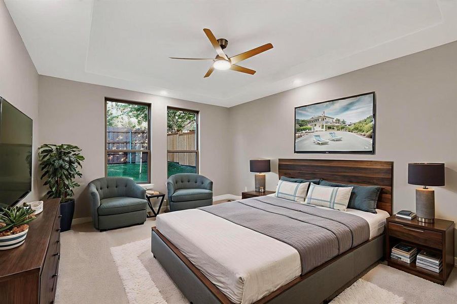 Bedroom with light carpet, a ceiling fan, and a tray ceiling