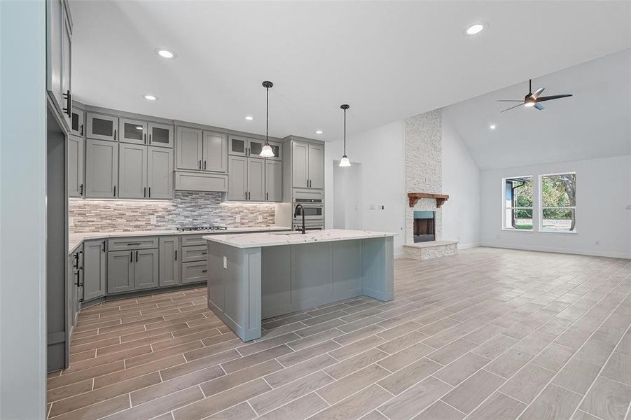 Kitchen with gray cabinetry, a center island with sink, backsplash, glass insert cabinets, and high vaulted ceiling Kitchen with gray cabinetry, a center island with sink, backsplash, glass insert cabinets, and high vaulted ceiling
