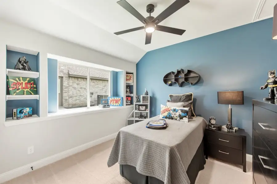 Children's bedroom with blue accent wall, Batman decor, built-in shelves, and ceiling fan