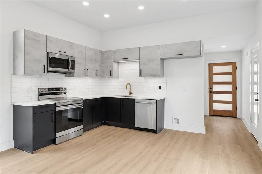 Kitchen featuring stainless steel appliances, tasteful backsplash, light countertops, light wood finished floors, and recessed lighting