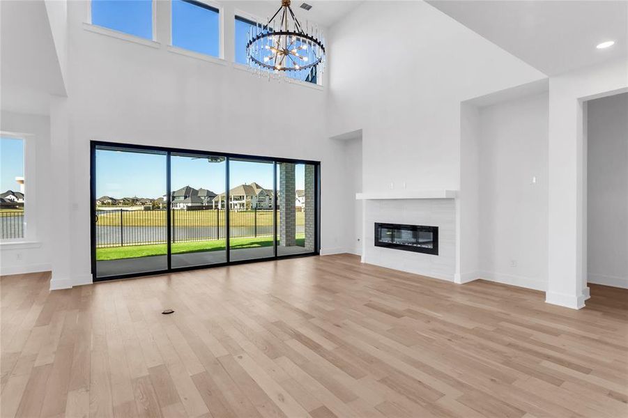 Unfurnished living room with light wood-type flooring, a residential view, a glass covered fireplace, a towering ceiling, and a chandelier