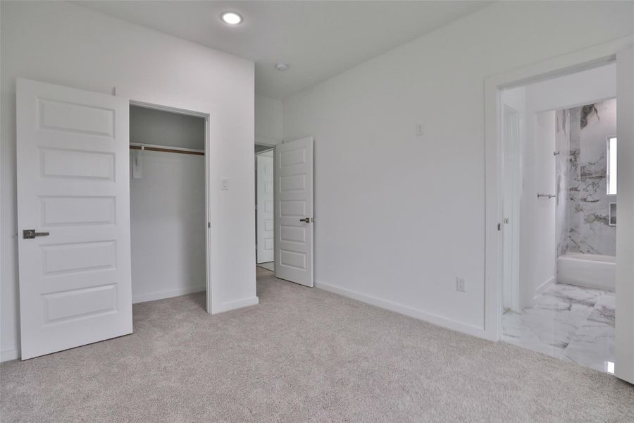 Bright bedroom with carpeted floors, a spacious closet, and an ensuite bathroom featuring elegant marble tiles.
