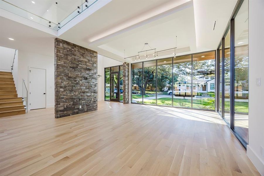Unfurnished living room with a wall of windows, light wood-style flooring, a tray ceiling, and stairway Unfurnished living room with a wall of windows, light wood-style flooring, a tray ceiling, and stairway