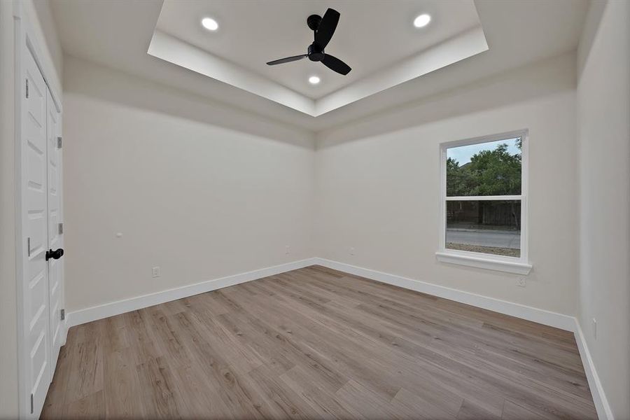 Empty room featuring a tray ceiling, light wood-type flooring, recessed lighting, and a ceiling fan
