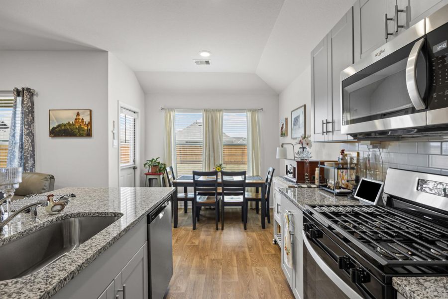 Kitchen featuring stainless steel appliances, lofted ceiling, light stone countertops, gray cabinetry, and light wood-type flooring