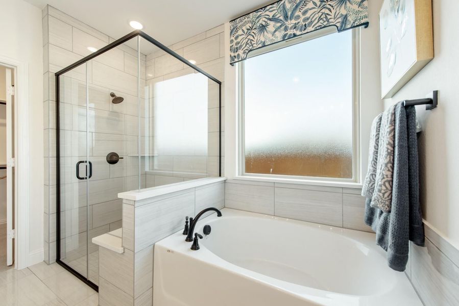 Master bathroom with soaking tub, glass-enclosed shower, white tile walls, and black fixtures near a frosted window Master bathroom with soaking tub, glass-enclosed shower, white tile walls, and black fixtures near a frosted window