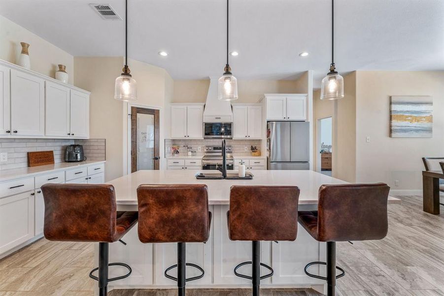 Kitchen with white cabinetry, tasteful backsplash, a kitchen island with sink, decorative light fixtures, and recessed lighting Kitchen with white cabinetry, tasteful backsplash, a kitchen island with sink, decorative light fixtures, and recessed lighting