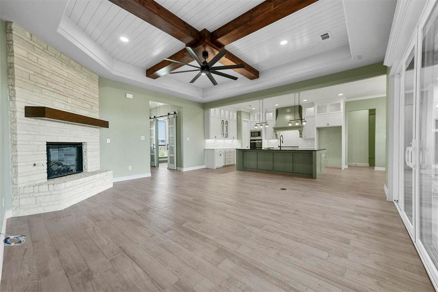 Unfurnished living room featuring sink, ceiling fan, a barn door, a fireplace, and light hardwood / wood-style floors