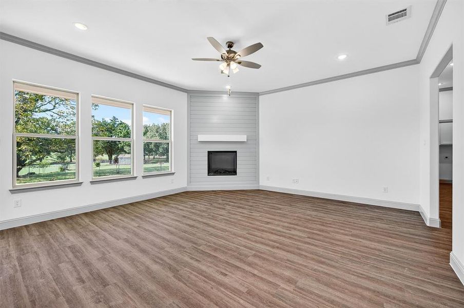 Unfurnished living room with crown molding, light wood-type flooring, a large fireplace, recessed lighting, and a ceiling fan