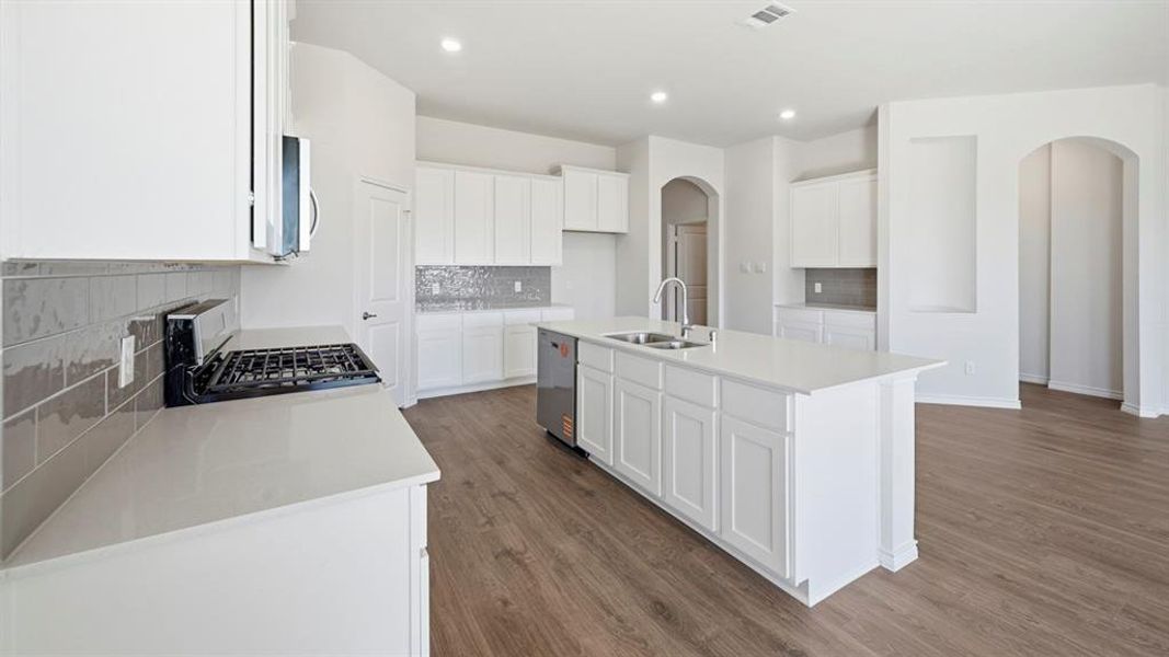 Modern kitchen featuring white cabinetry, light countertops, wood-finish flooring, a kitchen island with a double sink, and stainless steel appliances