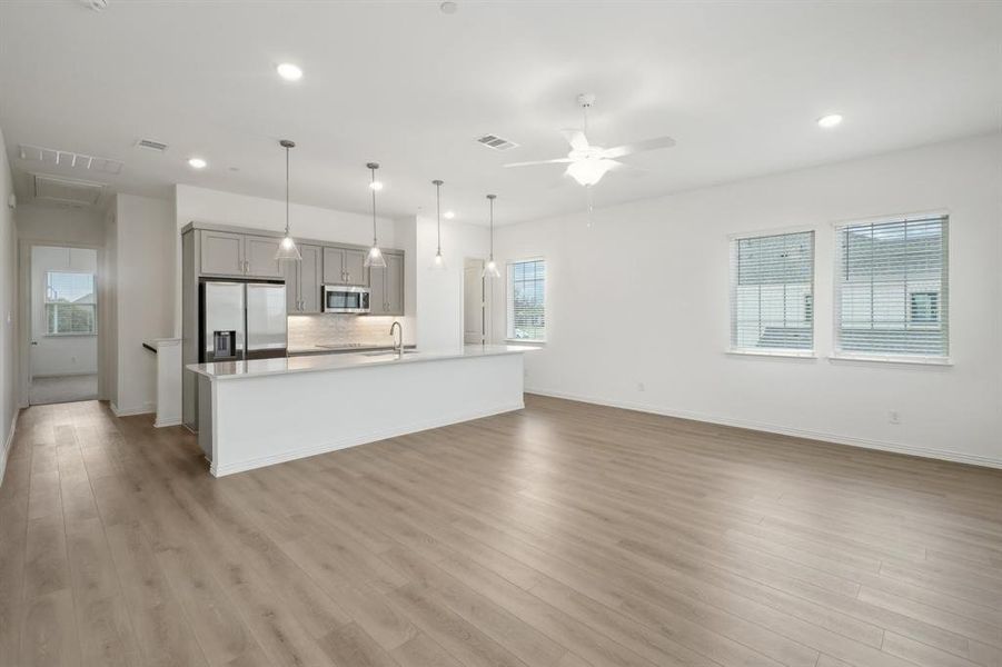 Kitchen featuring gray cabinetry, stainless steel appliances, pendant lighting, light hardwood / wood-style floors, and a kitchen island with sink