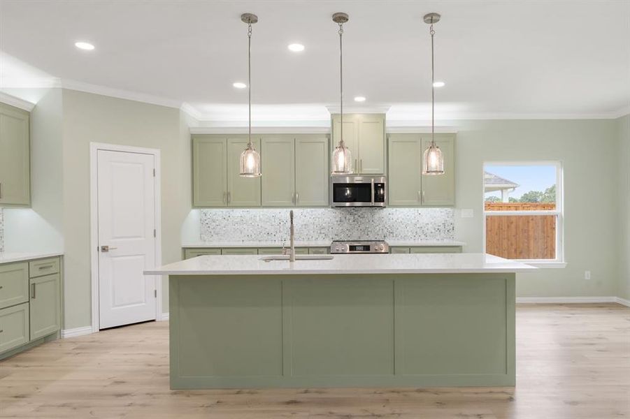 Kitchen with light hardwood / wood-style floors, a kitchen island with sink, green cabinetry, and backsplash