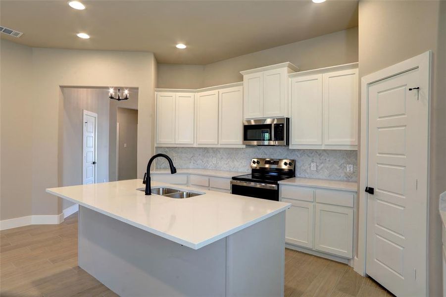 Kitchen with white cabinetry, tasteful backsplash, appliances with stainless steel finishes, an island with sink, and light wood finished floors Kitchen with white cabinetry, tasteful backsplash, appliances with stainless steel finishes, an island with sink, and light wood finished floors