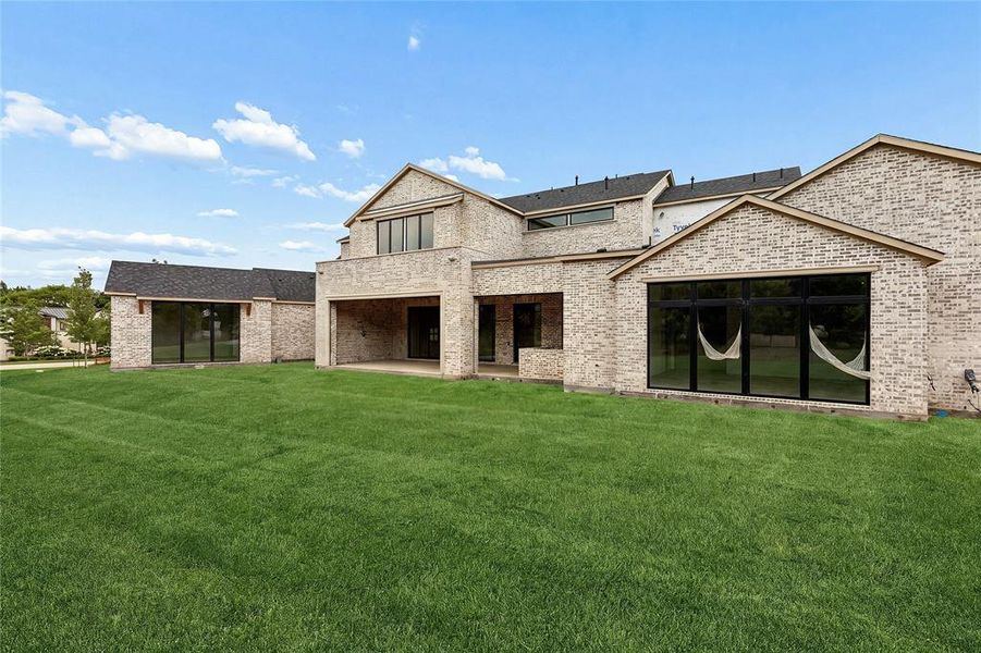 Expansive green lawn bordering a modern brick exterior with multiple large windows, a covered patio, and a gabled roofline