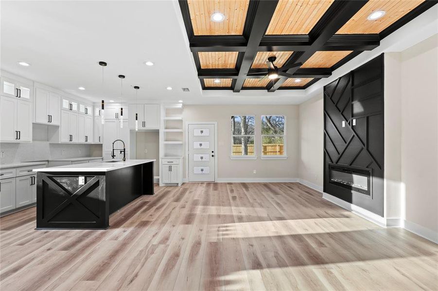 Kitchen with beam ceiling, white cabinetry, an island with sink, pendant lighting, and light wood-type flooring