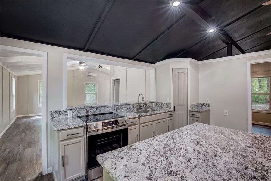 Kitchen featuring stainless steel electric stove, sink, vaulted ceiling with beams, and light stone counters