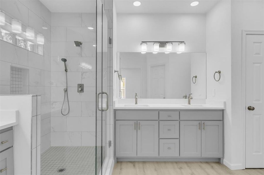 Full bath featuring double vanity, a shower stall, light wood-style flooring, and recessed lighting
