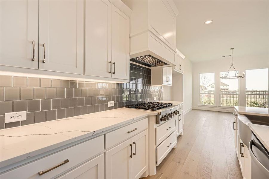 Kitchen featuring appliances with stainless steel finishes, light wood-type flooring, tasteful backsplash, pendant lighting, and white cabinetry