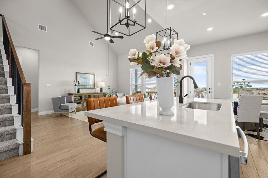 Kitchen featuring light stone countertops, a kitchen island with sink, light wood-type flooring, high vaulted ceiling, and pendant lighting