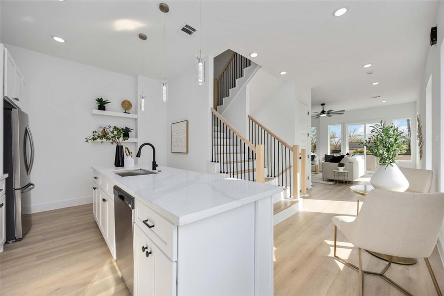 A bright, open kitchen features sleek white cabinetry, polished white quartz countertops, a stylish glossy subway-tile backsplash, and a spacious quartz-topped island with a matte black faucet that anchors the modern, airy layout overlooking the adjacent living and dining areas.