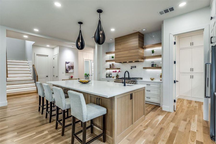 Kitchen featuring premium range hood, a center island with sink, white cabinets, light hardwood / wood-style floors, and stainless steel refrigerator