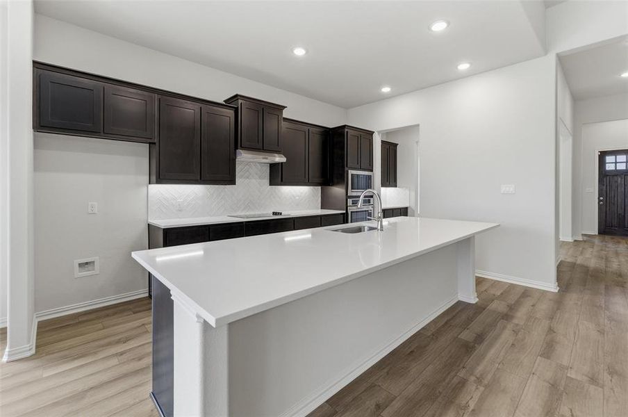 Kitchen with backsplash, a kitchen island with sink, light wood-style floors, stainless steel appliances, and recessed lighting