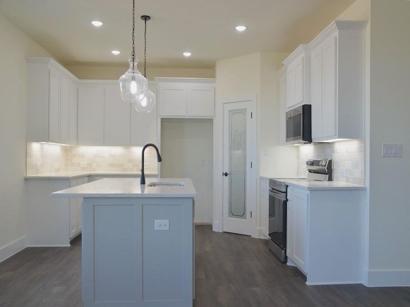 Kitchen featuring sink, decorative light fixtures, stainless steel electric range, a center island with sink, and white cabinets