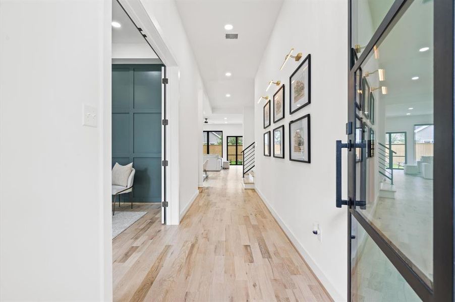 Bright entryway with oak flooring, a metal glass door, white walls, framed art, and a peek into a modern private office space. Clean design.