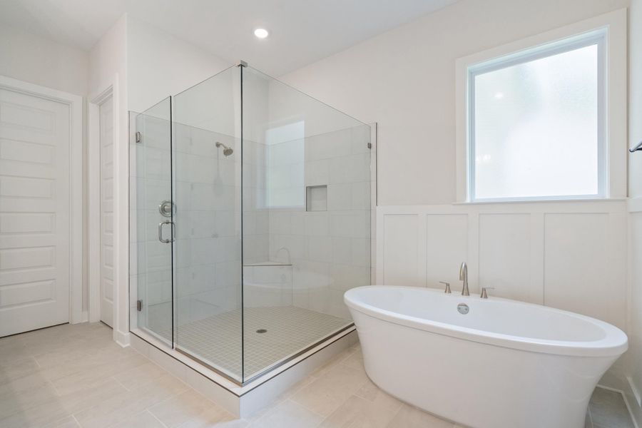 Freestanding soaking tub with brushed nickel fixtures, glass-enclosed shower with tile surround, built-in shower bench, and board and batten wall detailing
