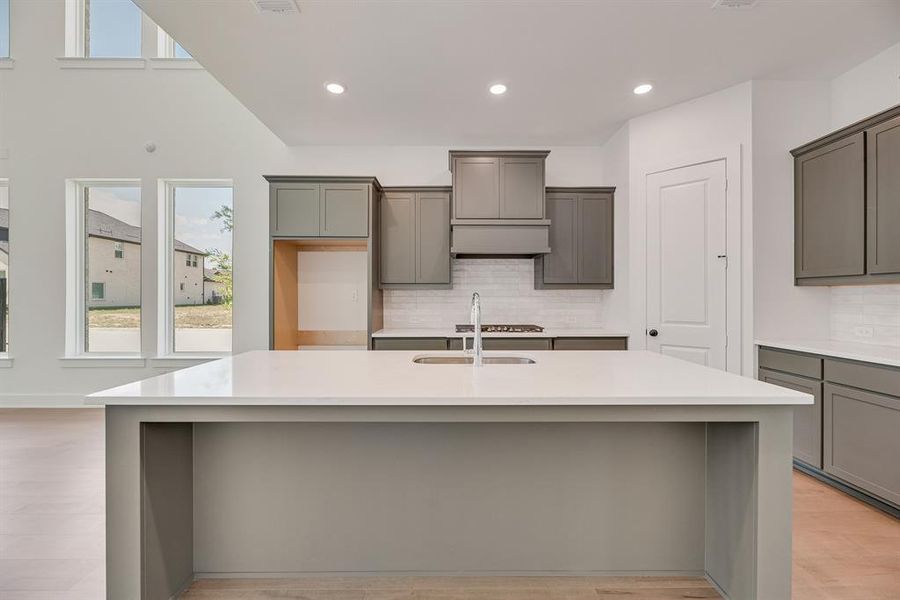 Kitchen with gray cabinetry, decorative backsplash, light stone counters, a center island with sink, and recessed lighting Kitchen with gray cabinetry, decorative backsplash, light stone counters, a center island with sink, and recessed lighting